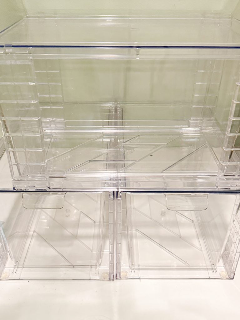 Four clear plastic storage bins are stacked in two rows against a light-colored wall, with the front doors slightly ajar.