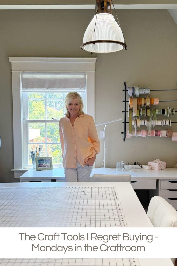 A woman stands in a well-lit craft room with shelves of ribbon and a large worktable. Text reads: "The Craft Tools I Regret Buying - Mondays in the Craftroom.
