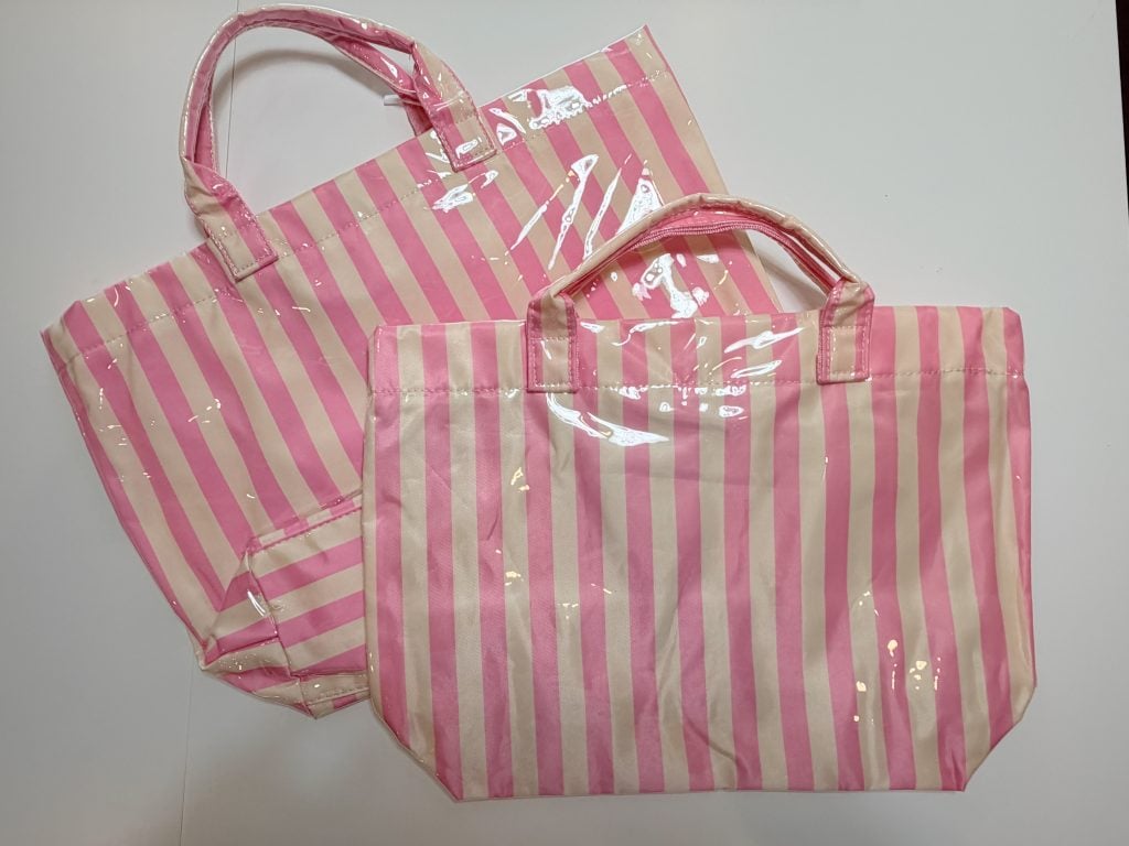 Two pink and white striped tote bags with handles are placed on a white surface. The bags have a glossy, plastic-coated finish.