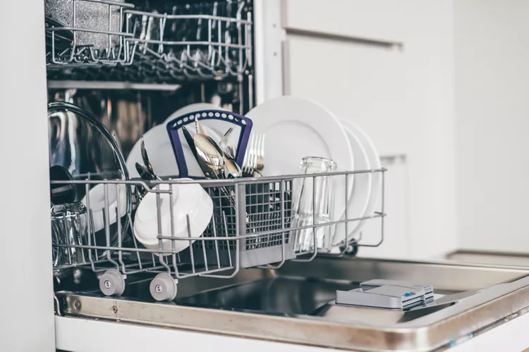 An open dishwasher with clean dishes, including plates, cups, glasses, and cutlery, organized in the racks.