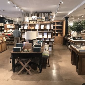 A retail store interior with wooden shelves, books, home decor items, and a person browsing in the background under ceiling track lighting.