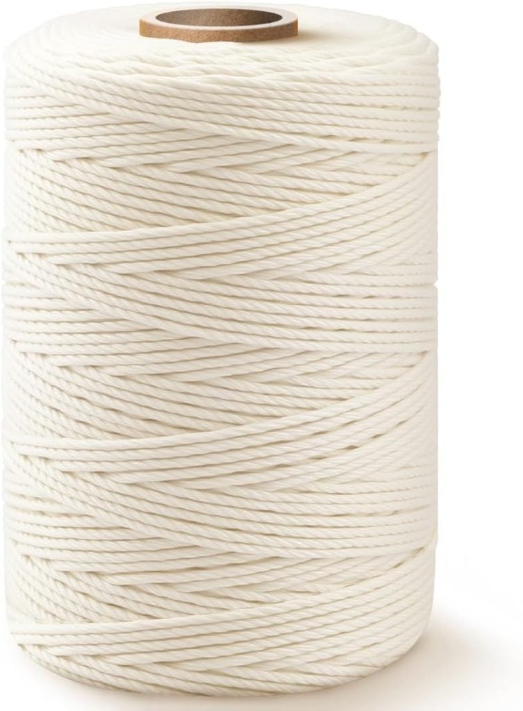 A large spool of white cotton twine is shown standing upright, with tightly wound strands and a visible cardboard core at the top.