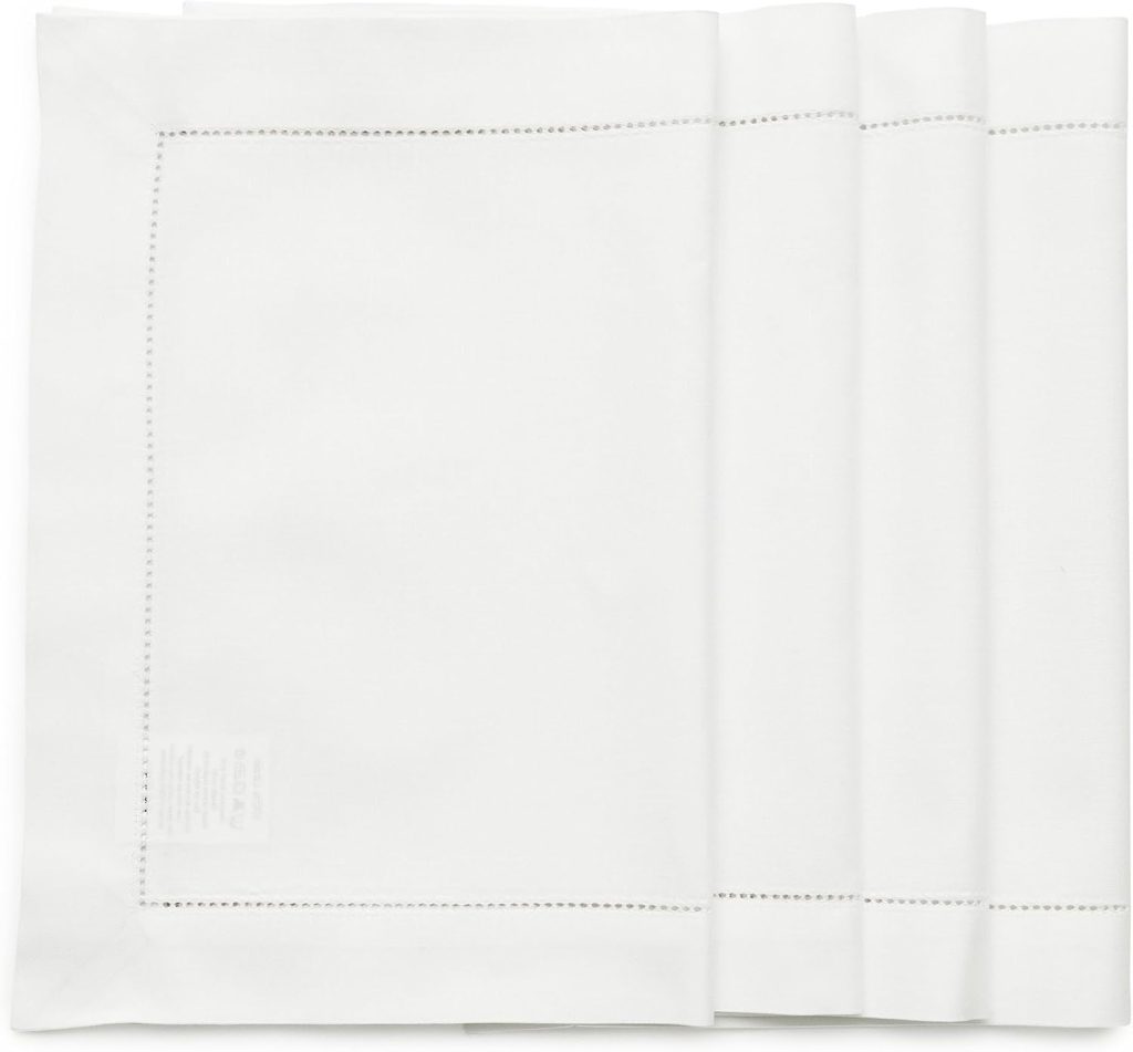 Four neatly folded white cloth napkins with simple stitched borders are arranged side by side on a flat surface.