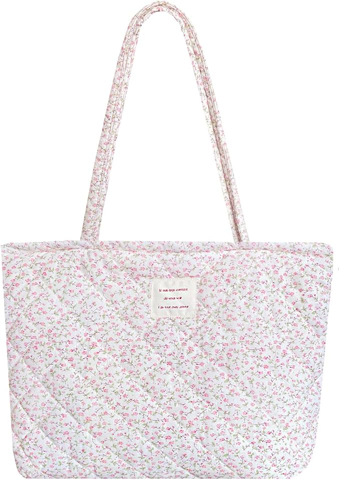 A quilted tote bag with long handles and a white background featuring a small pink floral pattern and a rectangular patch on the front.