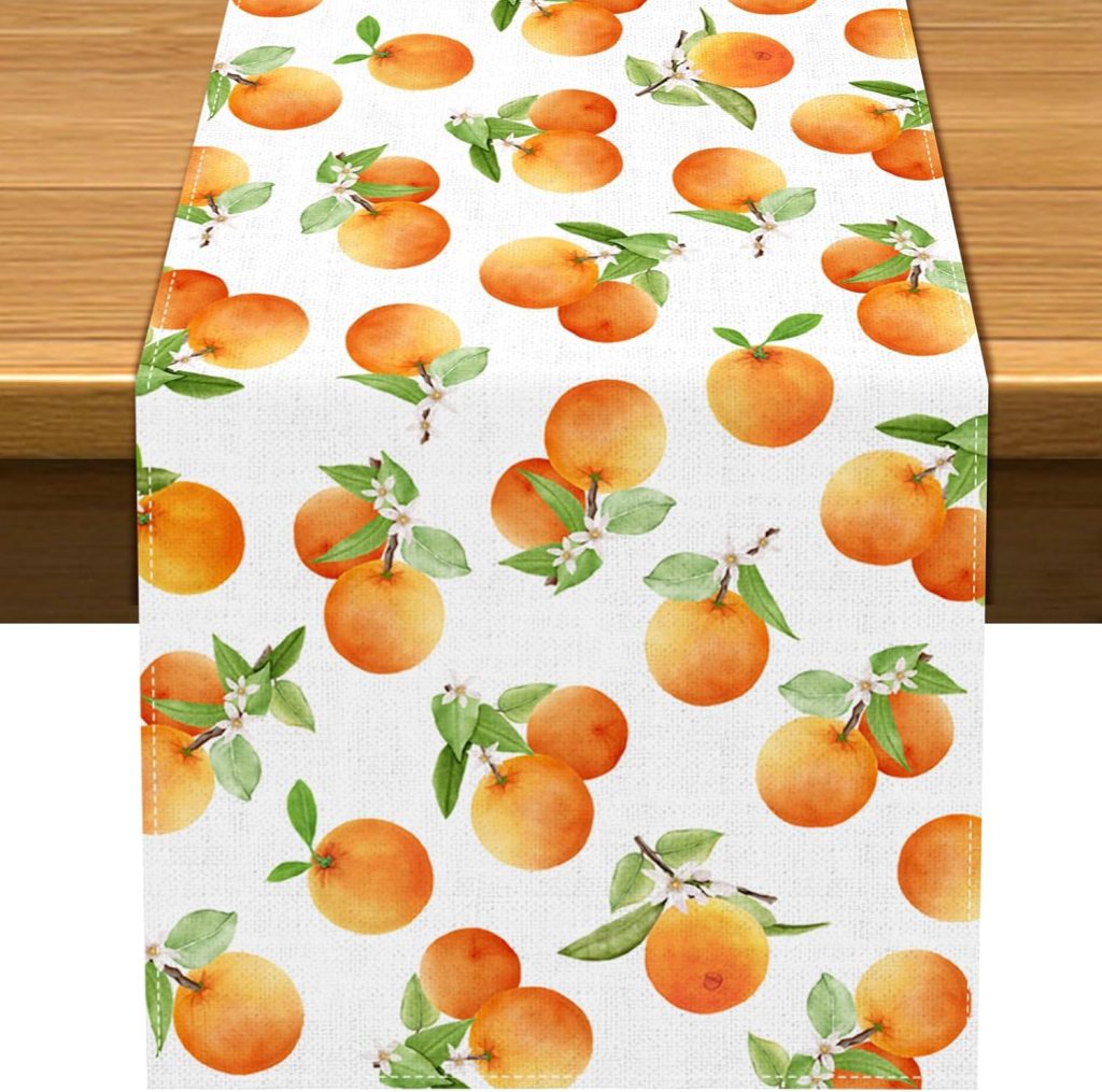 White table runner with a pattern of oranges, green leaves, and small white blossoms, draped over a wooden table.