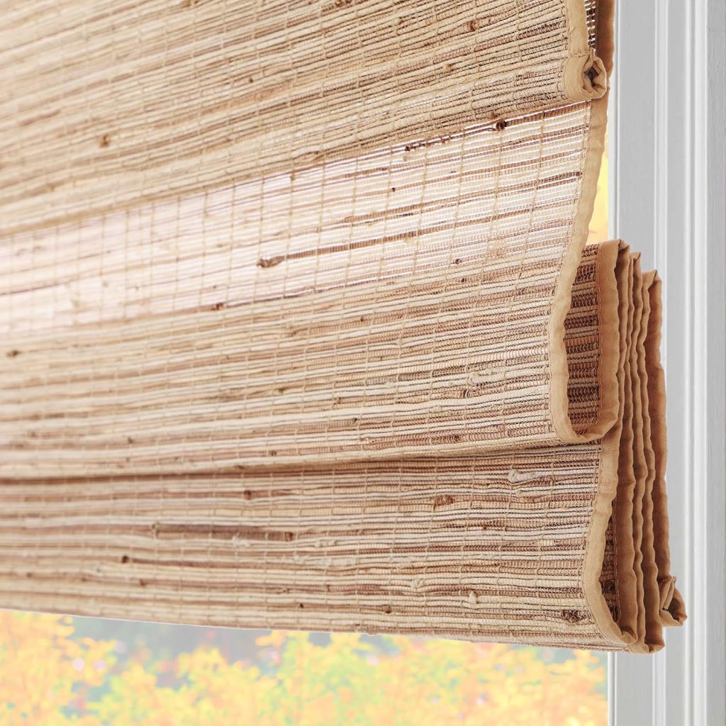 Close-up of a partially raised bamboo window shade with sunlight filtering through, showing the woven texture and edges. A hint of outdoor foliage and rattan furniture is visible in the background.