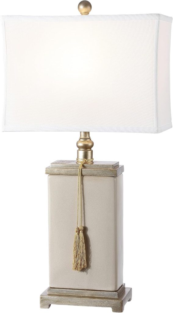 Rectangular table lamp with a white shade, gold finial, beige rectangular base, gold accents, and a gold decorative tassel hanging from the neck.