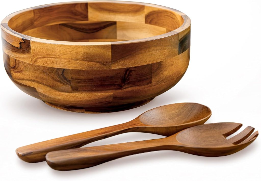 A wooden salad bowl with a matching wooden serving spoon and fork placed in front of it on a white background, perfect for serving a fresh grilled peach salad.