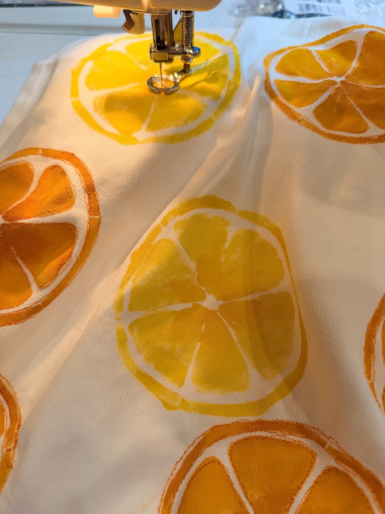 A sewing machine stitches fabric with a citrus fruit print, showing yellow and orange slices on a white background.