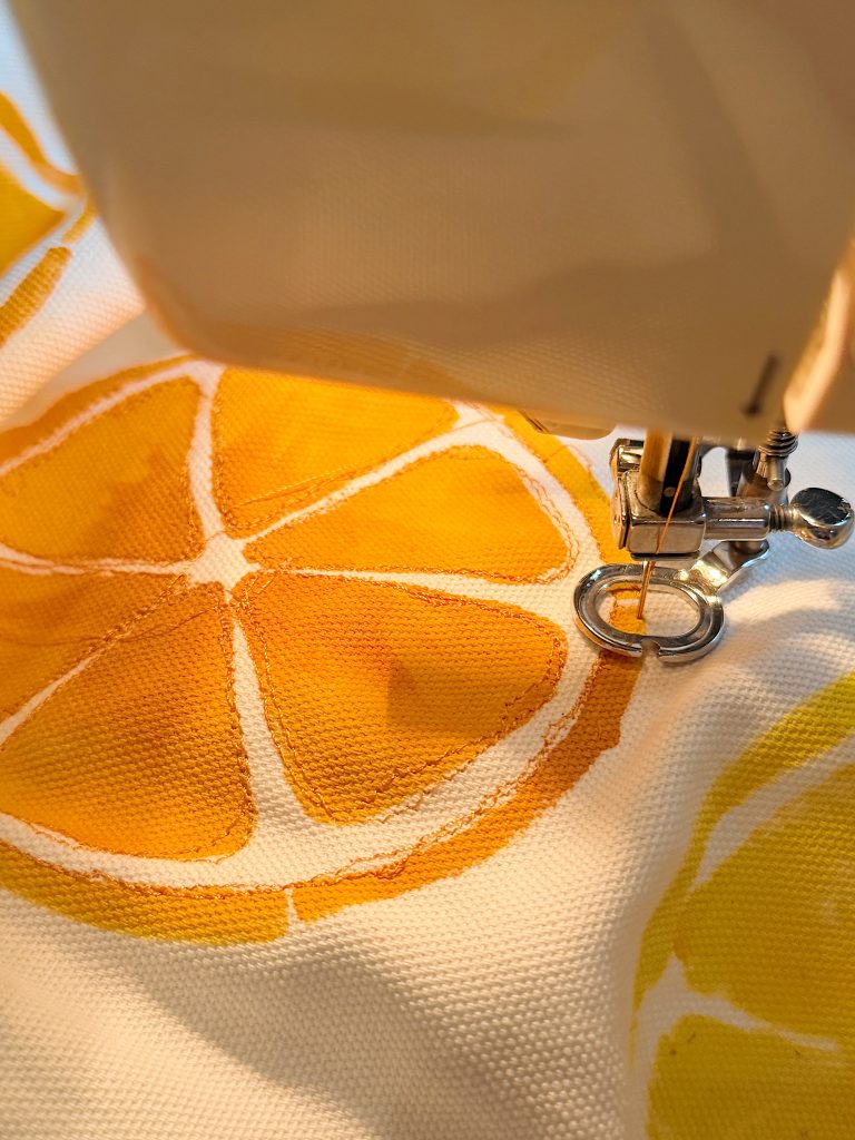 Close-up of a sewing machine stitching fabric with a printed orange slice pattern under the needle.