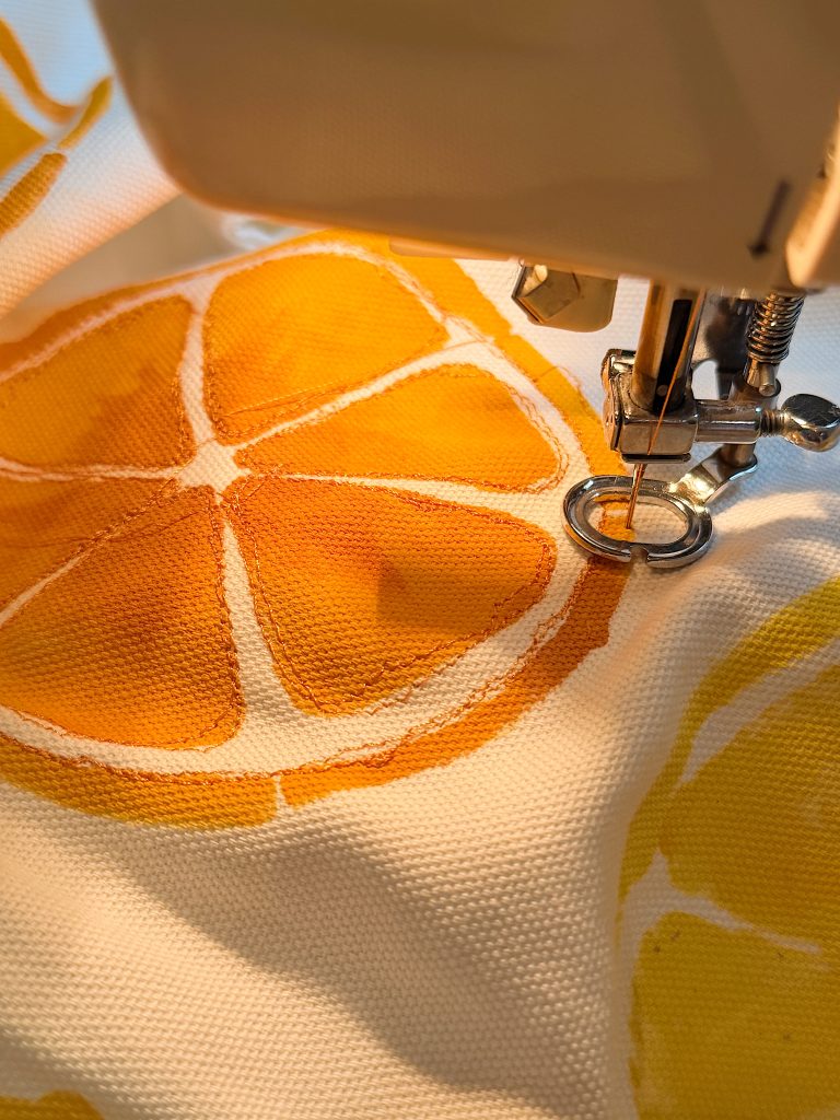 A sewing machine needle works on fabric with an orange slice print, highlighting the stitching process and textile details.