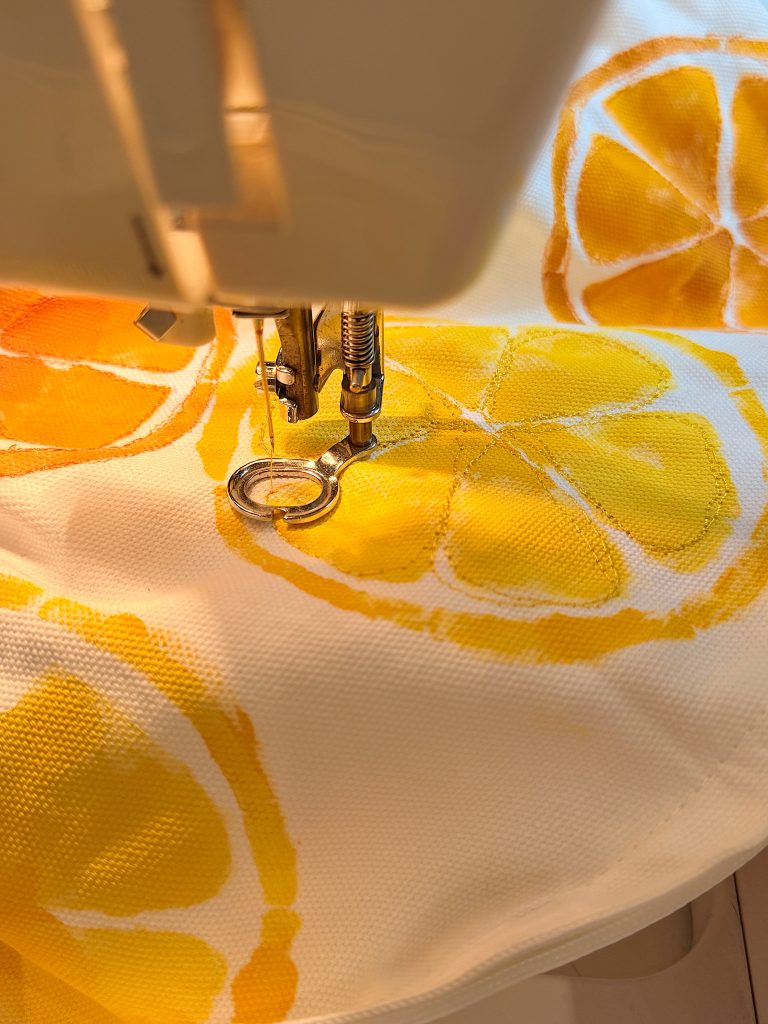 Close-up of a sewing machine needle stitching yellow citrus-printed fabric.