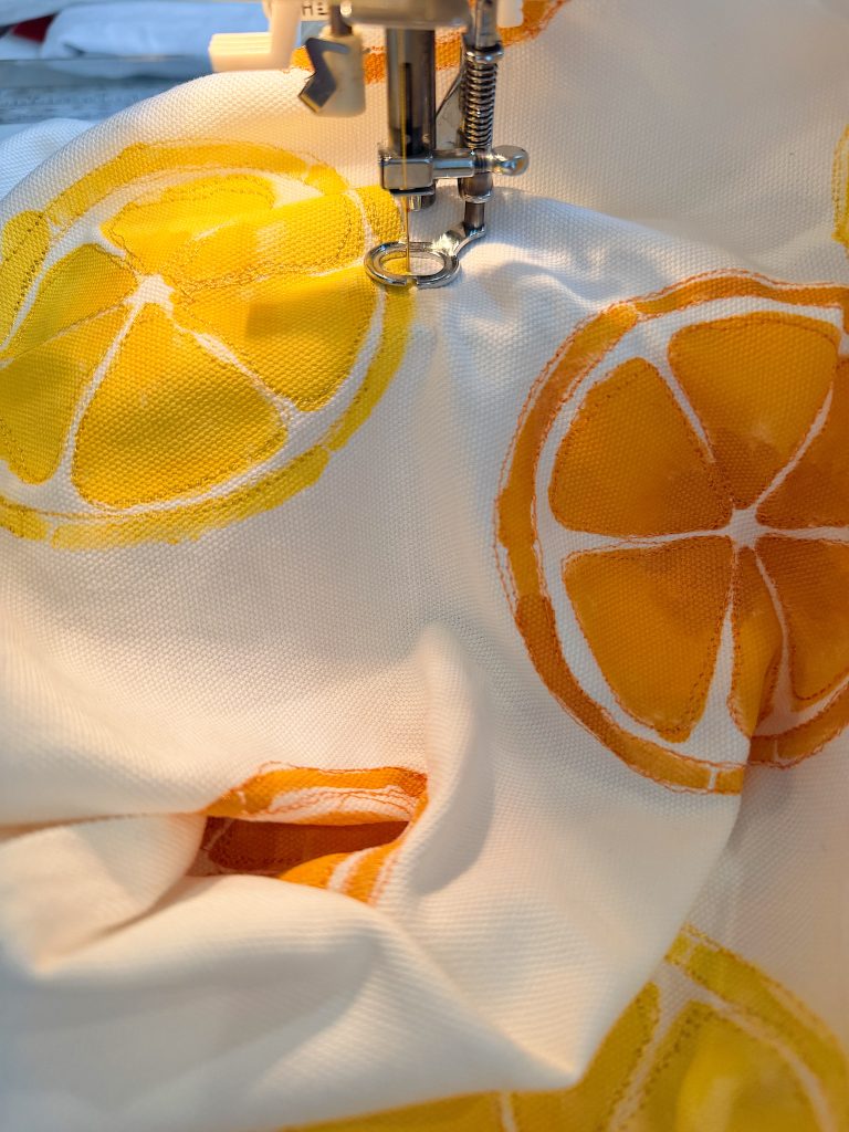 A sewing machine stitches white fabric printed with orange and yellow citrus slices.