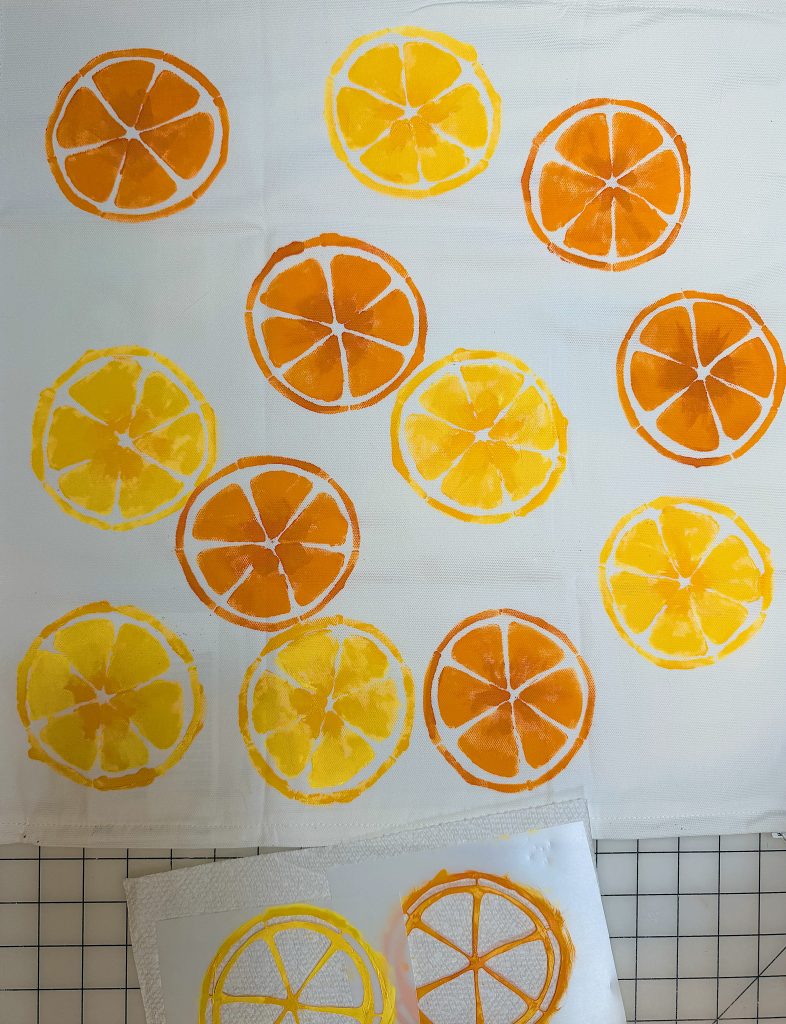 Cloth with orange and yellow citrus slice prints arranged randomly; two stencils with similar designs are placed at the bottom.