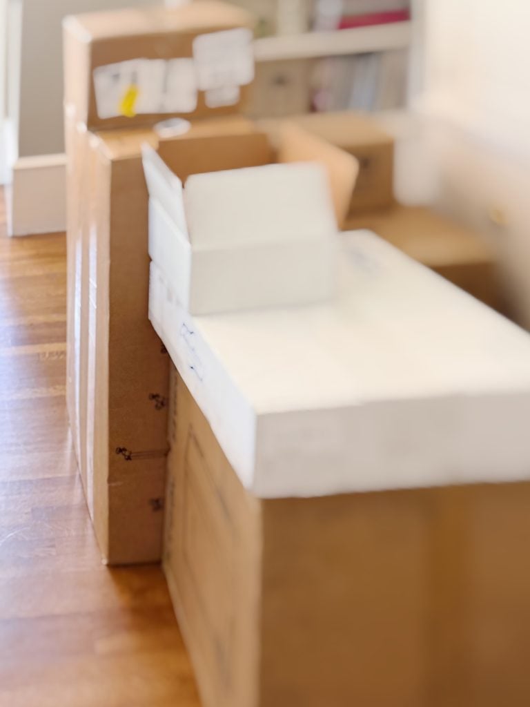 Several cardboard boxes, some open and some closed, are arranged on a hardwood floor in a well-lit room.