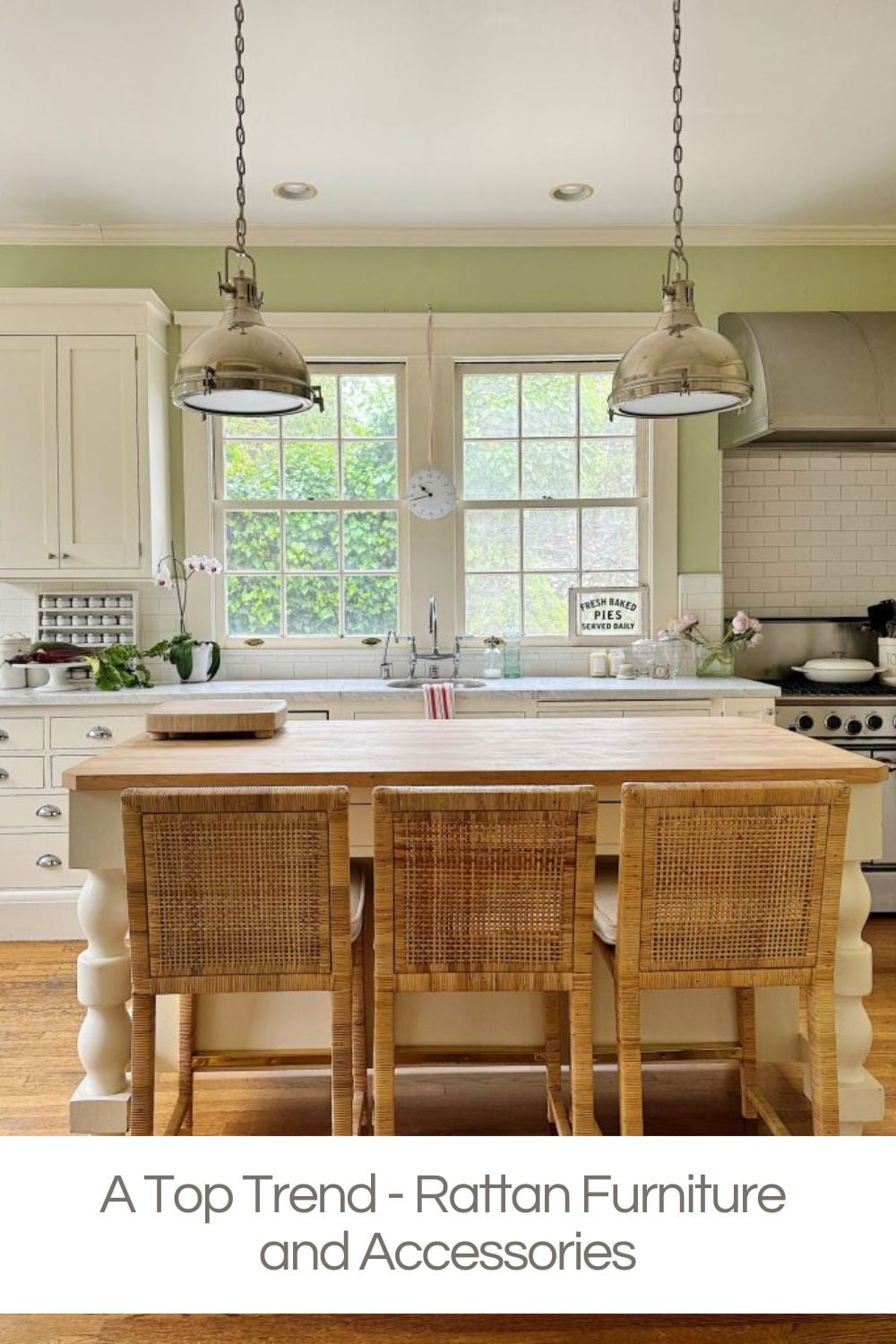 A kitchen with white cabinets, a wooden island, three rattan bar stools that beautifully showcase rattan furniture, pendant lights, and green walls.
