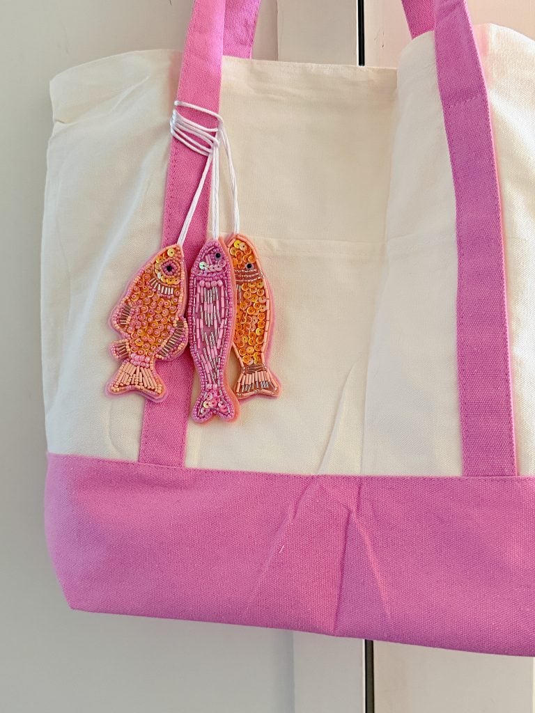 White and pink tote bag with two embroidered fish keychains attached to a handle.
