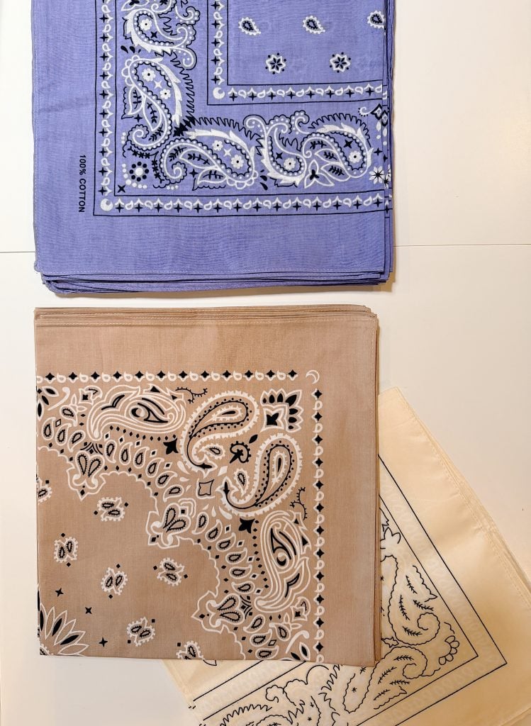 Three folded bandanas in blue, tan, and cream with paisley patterns arranged on a white surface.