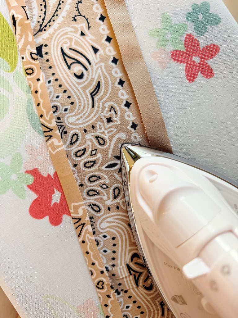 A close-up of an iron pressing a seam on patterned fabric with floral and paisley designs.