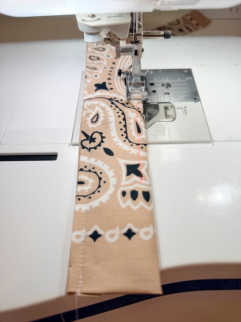A sewing machine stitching a seam on a piece of beige fabric with a black and white paisley pattern.