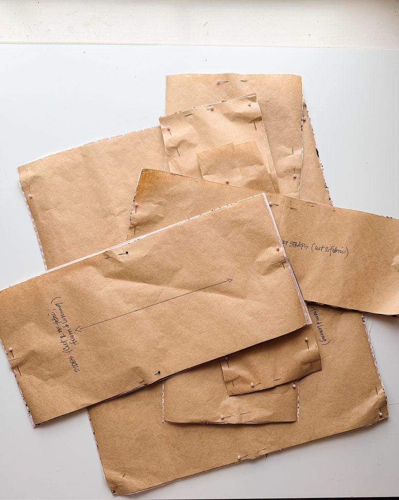 Several pieces of brown pattern paper, each pinned to fabric, are layered on a flat surface with handwritten notes and markings visible.