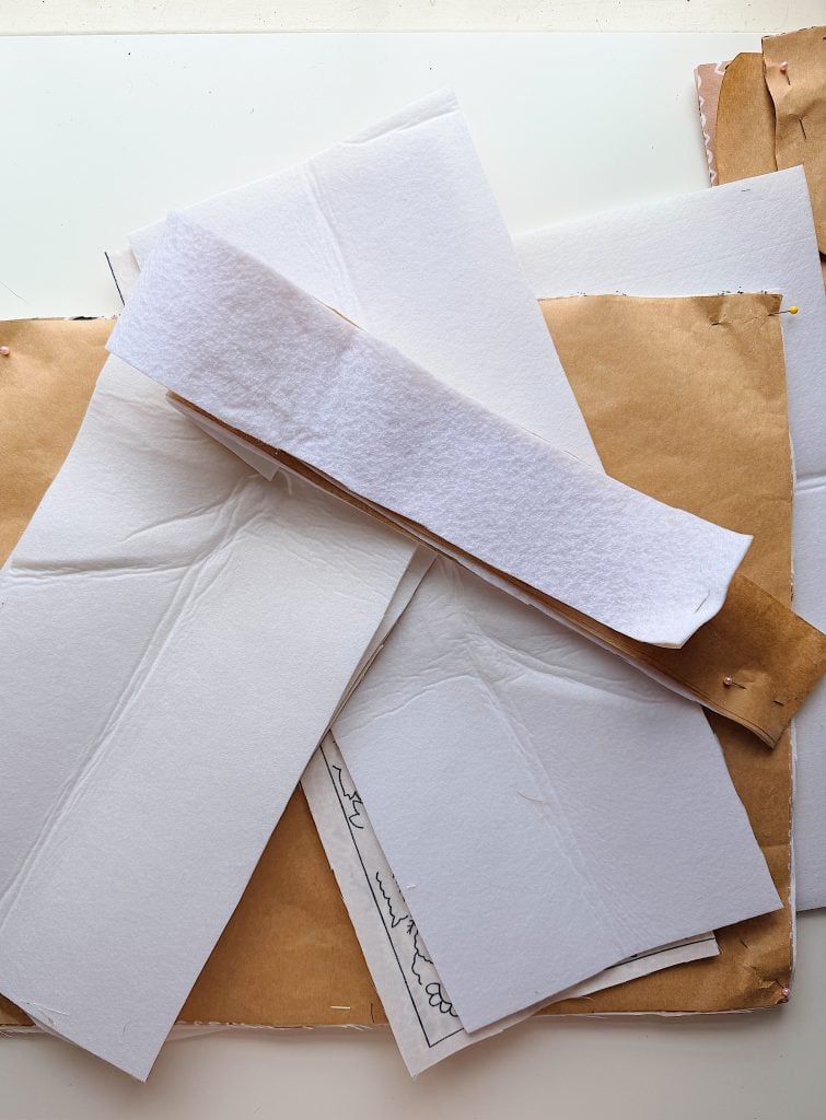 A stack of paperboard, white felt, and brown kraft paper sheets are layered on a white surface.