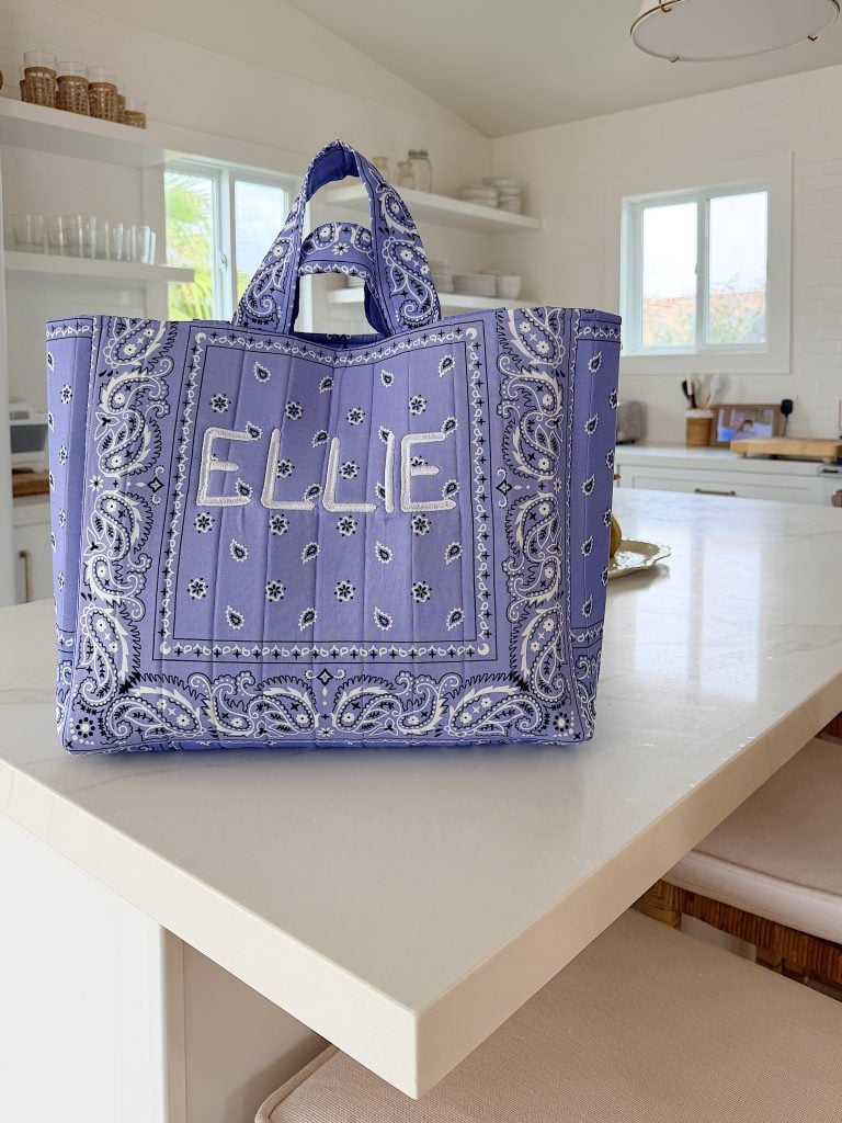 A purple and white bandana-patterned tote bag with the name "ELLE" on the front sits on a white kitchen counter in a bright, modern kitchen.