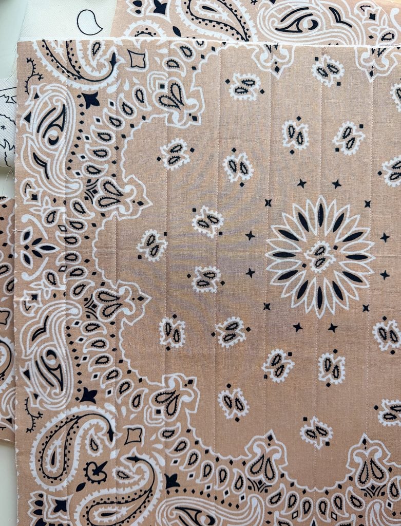 A close-up photo of tan-colored paper printed with a black and white paisley bandana pattern, featuring floral and ornamental motifs.