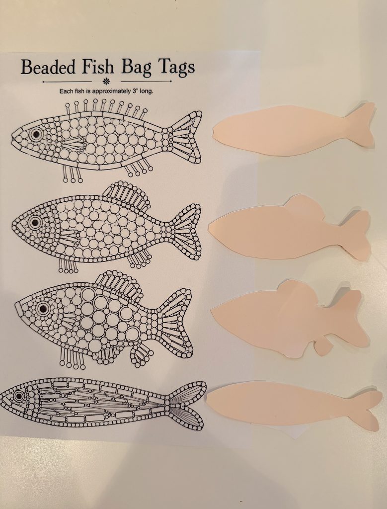 Four blank fish-shaped cutouts are placed next to a printed sheet with three beaded fish bag tag coloring templates.