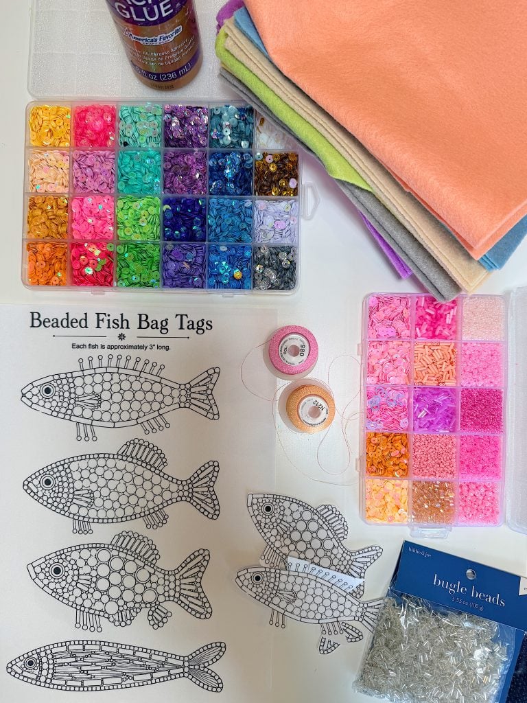 Assorted craft supplies, including beads, felt sheets, glue, thread, and four fish patterns labeled "Beaded Fish Bag Tags," are arranged on a white surface.