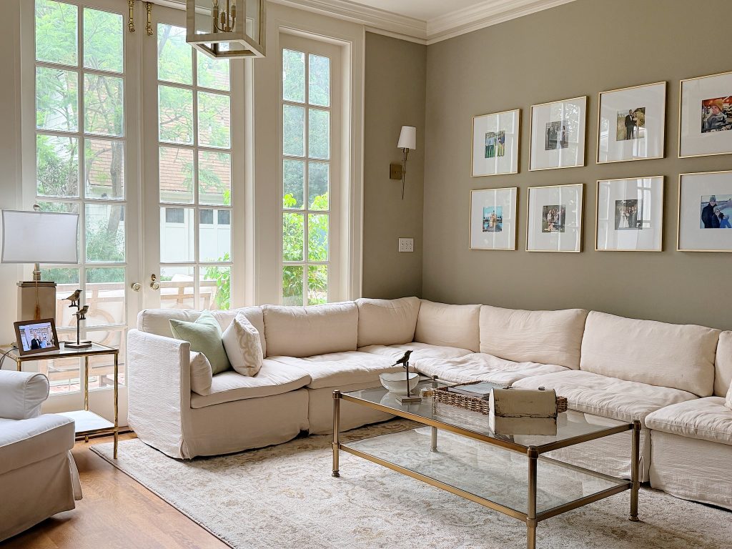 Bright living room with large windows, a white sectional sofa, glass coffee table, framed photos on the wall, and neutral-colored decor.