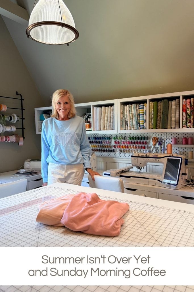 Woman standing in a well-organized sewing room with fabric, thread, and sewing machines; folded sweatshirts on the worktable. Text reads, "Summer Isn't Over Yet and Sunday Morning Coffee.