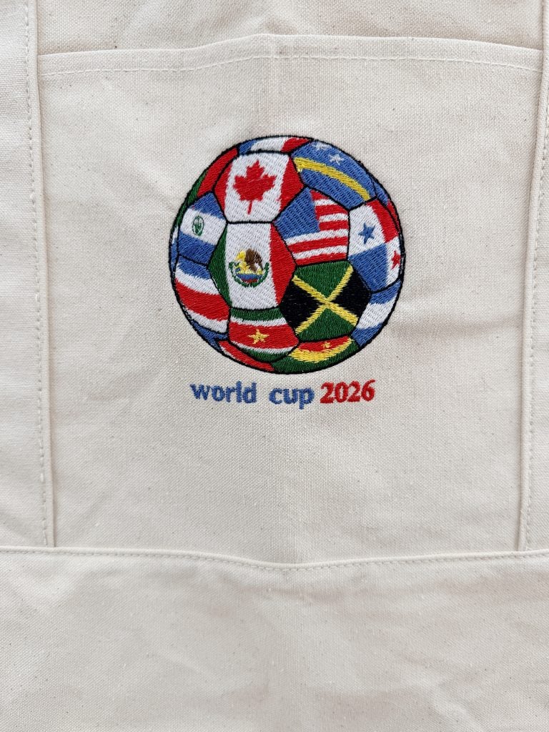 A soccer ball with various national flags and text "world cup 2026" embroidered on a beige fabric background.