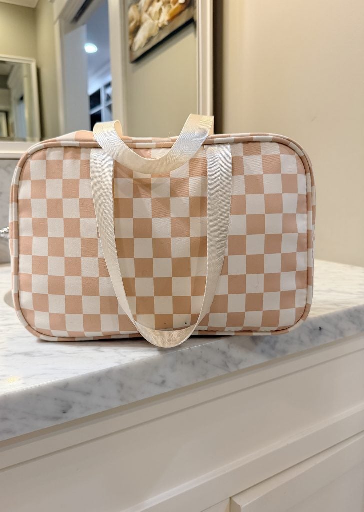 A rectangular bag with beige and white checkerboard pattern and white handles sits on a marble countertop.