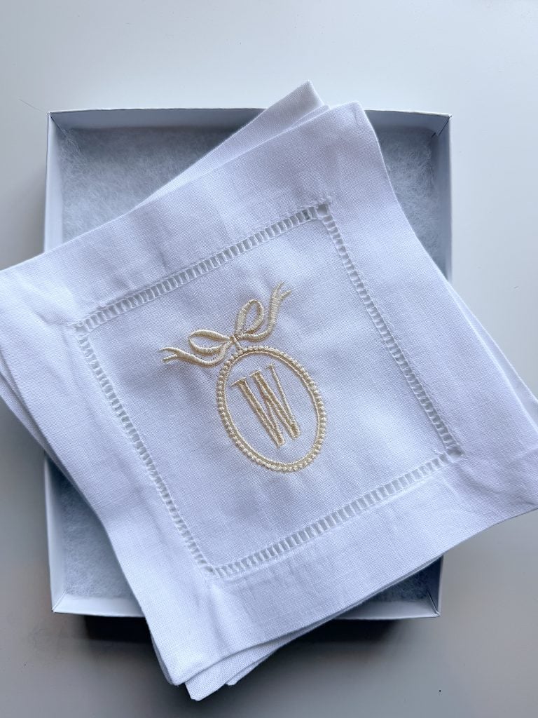 White handkerchief with an embroidered letter "W" inside an oval with a bow, placed neatly in an open white box.