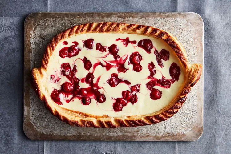 Oval-shaped pastry with braided crust, filled with creamy custard and swirled cherry topping, displayed on a decorative metal tray.